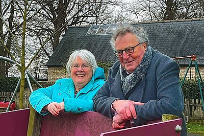 Lib Dem Candidates for Bottisham, Charlotte Cane and John Trapp, in a children's playground with a building in the background