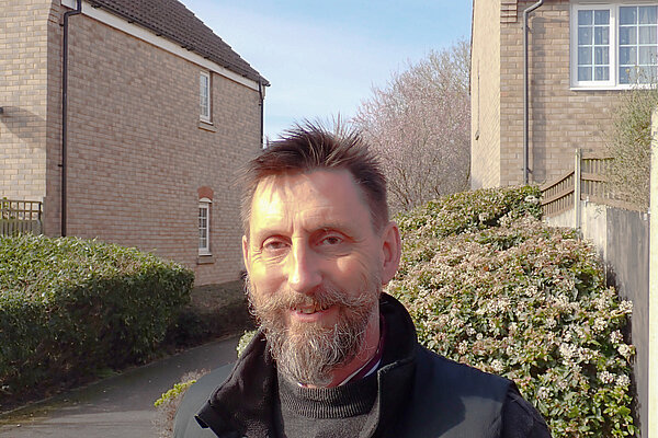 Head and shoulder image of Alec Jones with house in background and green bushes