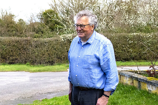 John Trapp standing on green grass near a road, with bushes and trees in the background